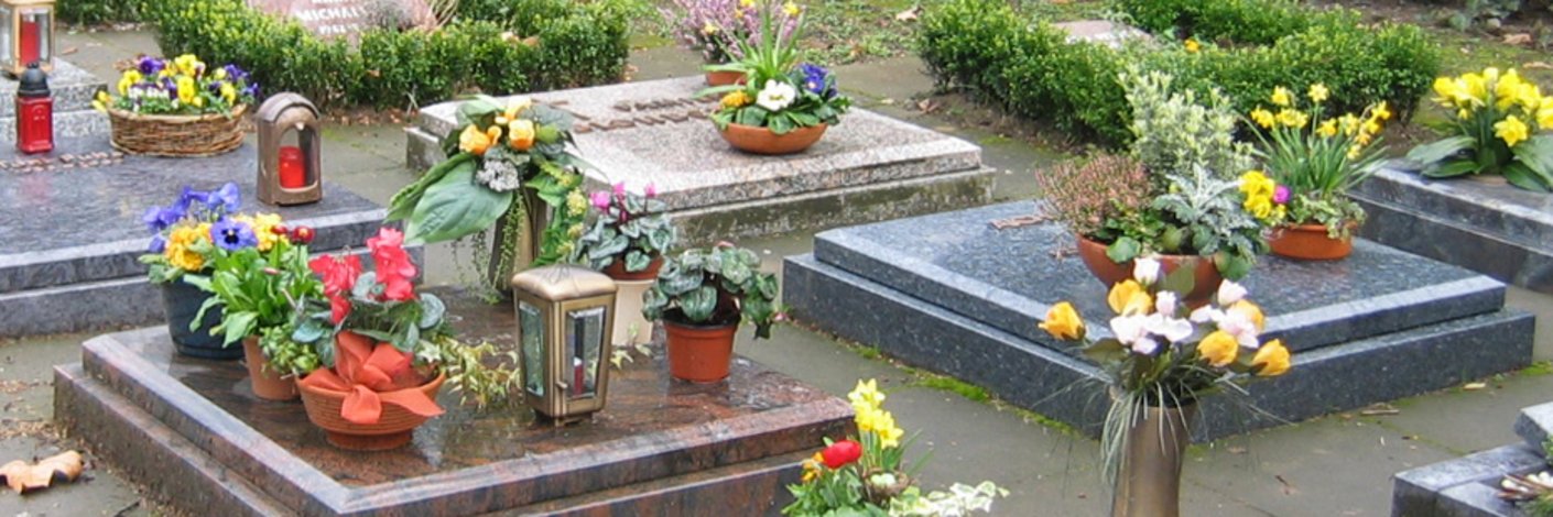 Urnengräber mit Grabplatten aus Stein und Blumenschmuck und Grablampen