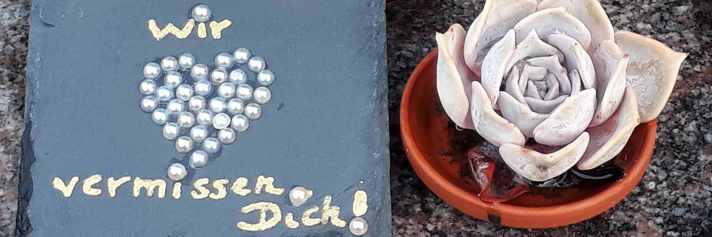 Grabschmuck in Form einer steinernen Blume, mit Perlen sowie Inschrift