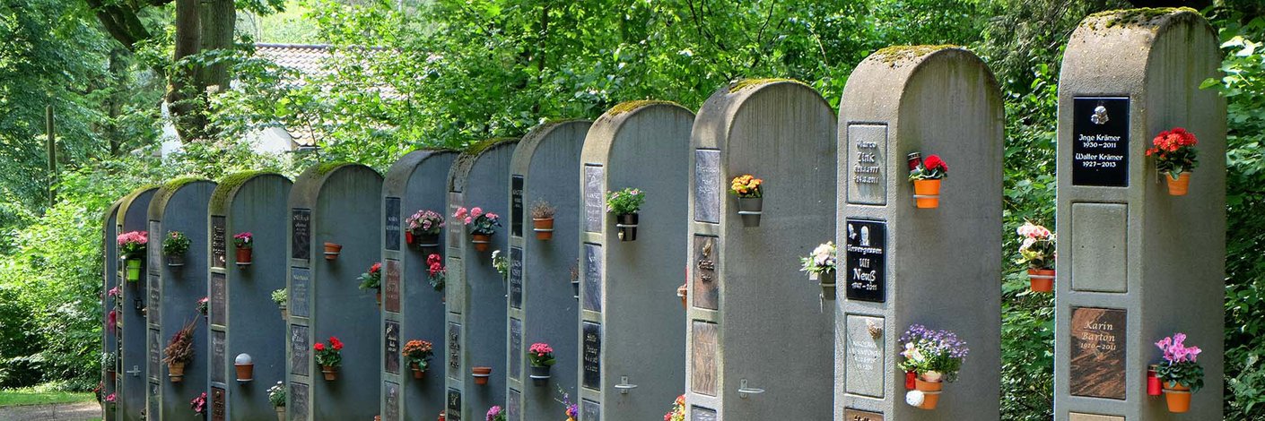 Urnenwand aus einzelnen grauen Stelen mit Abdeckplatten und Blumenschmuck