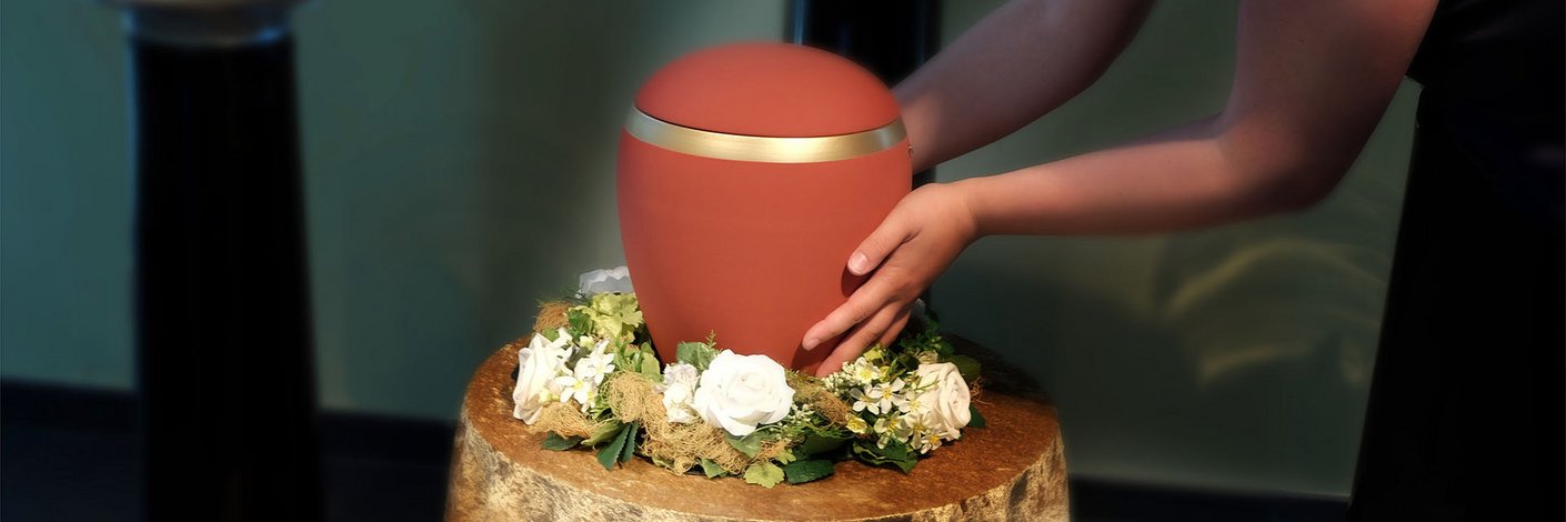 Frau umfasst eine rote Urne mit Blumenschmuck